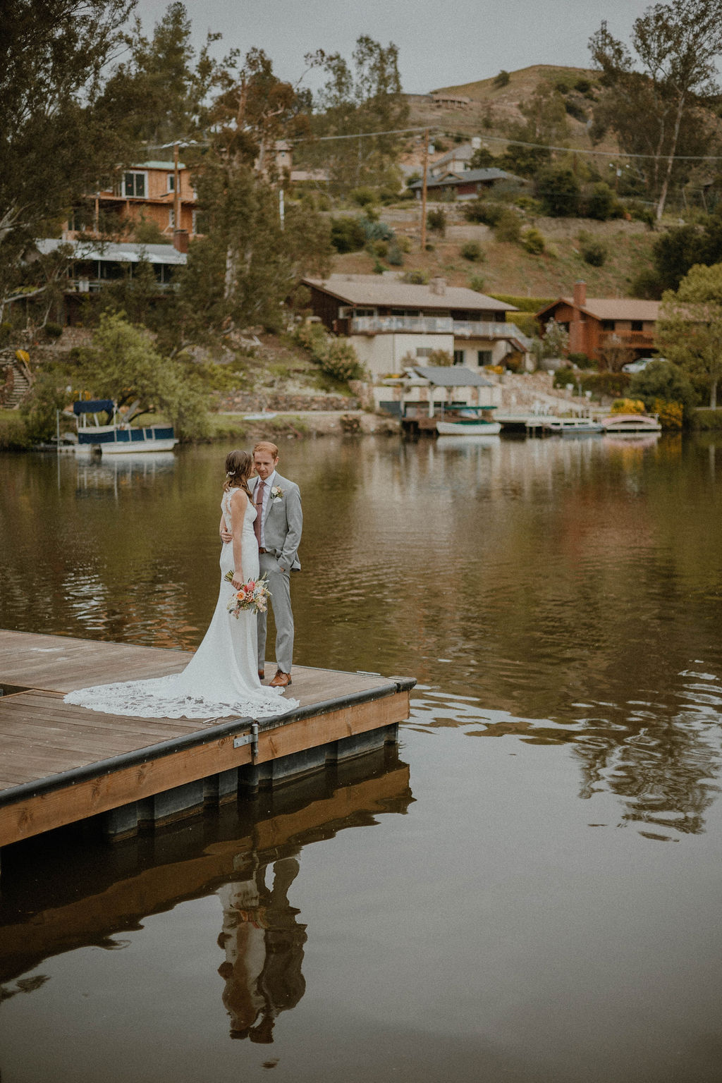 the bride and groom standing at the end of the dock