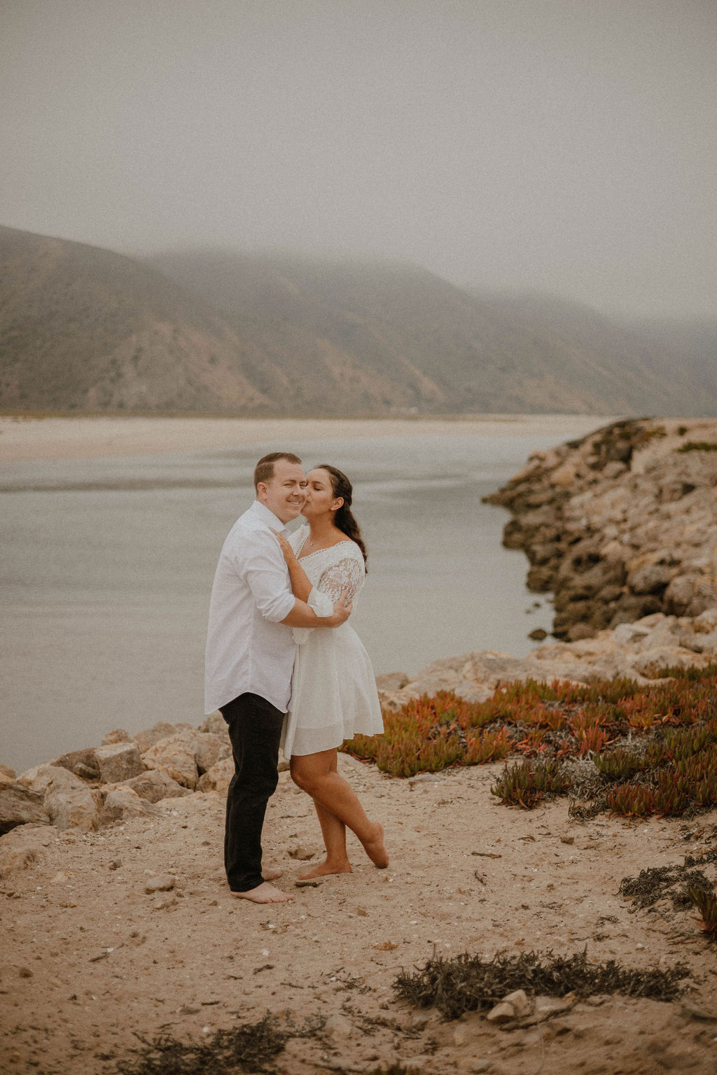 fiance kissing his cheek by the shoreline during their engagement pictures