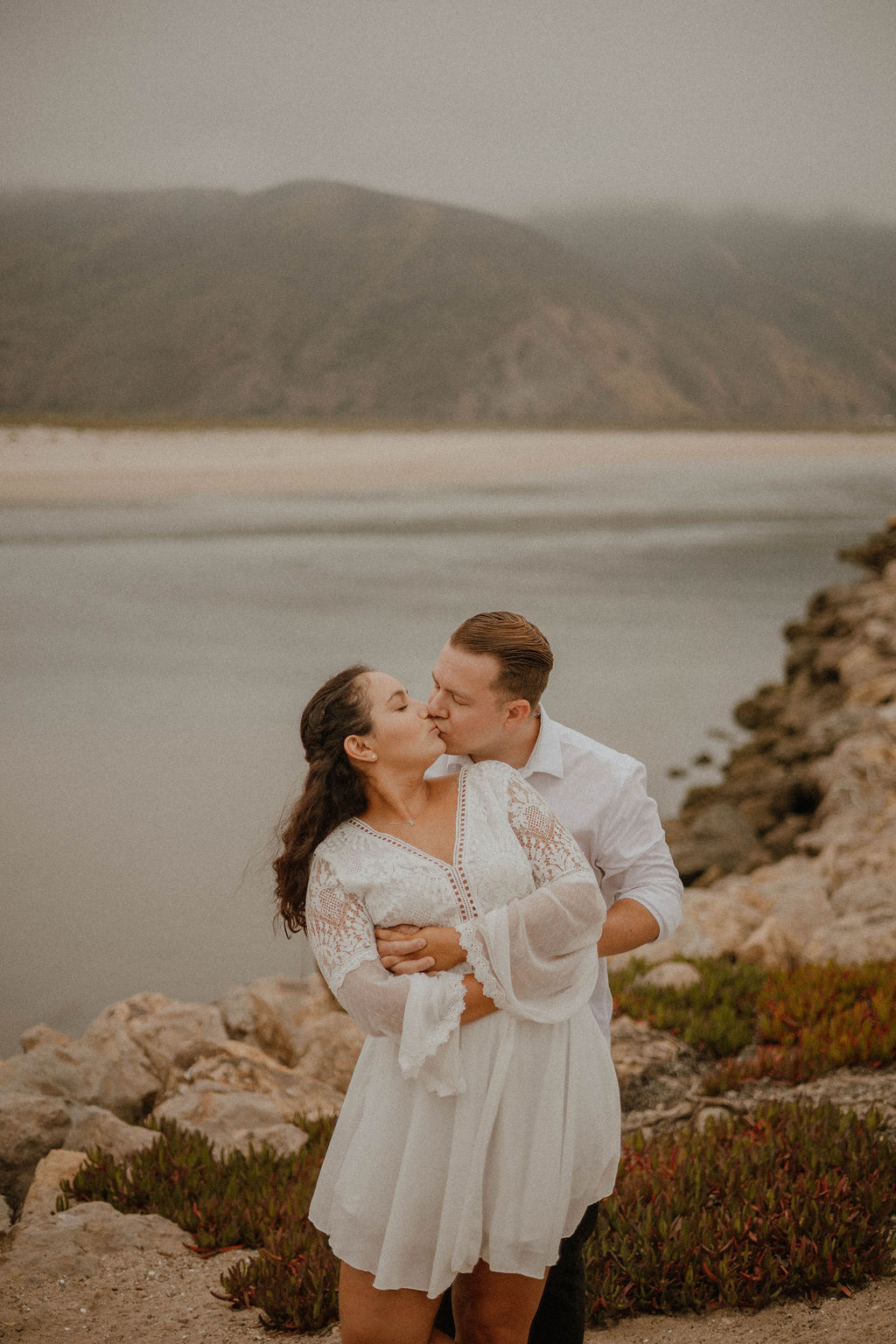 fiances kissing at on the rocks by the water at the Point Mugu Naval Base