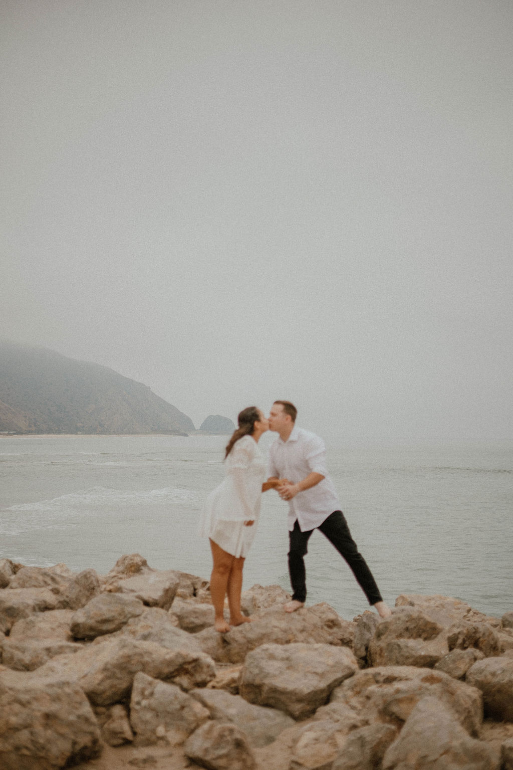 fiances kissing on the rocks during their beach engagement session