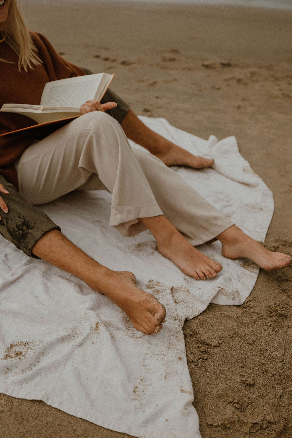 couples legs and books on a blanket in the sand