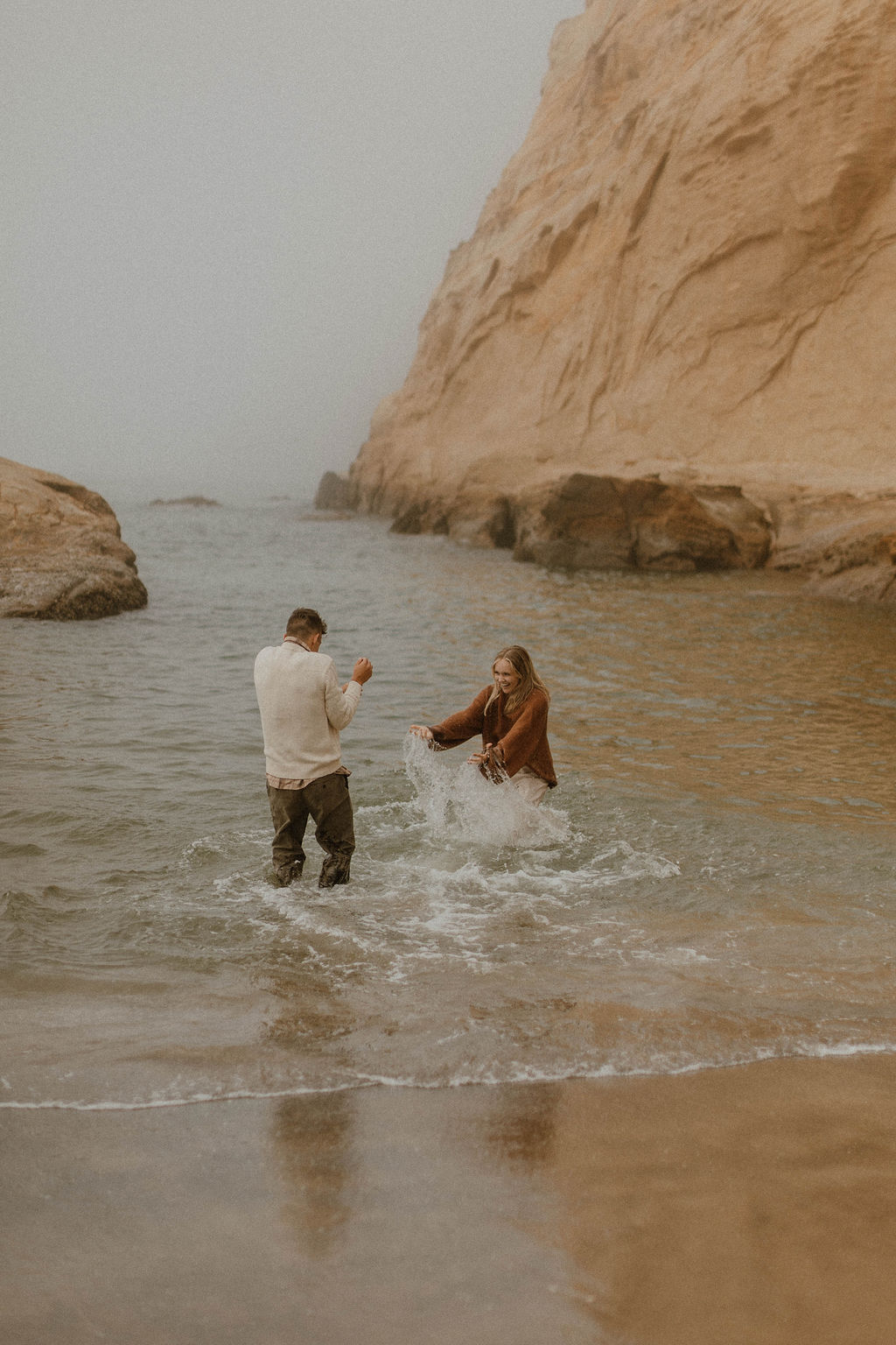 couple splashing each other in the water at their couples photoshoto