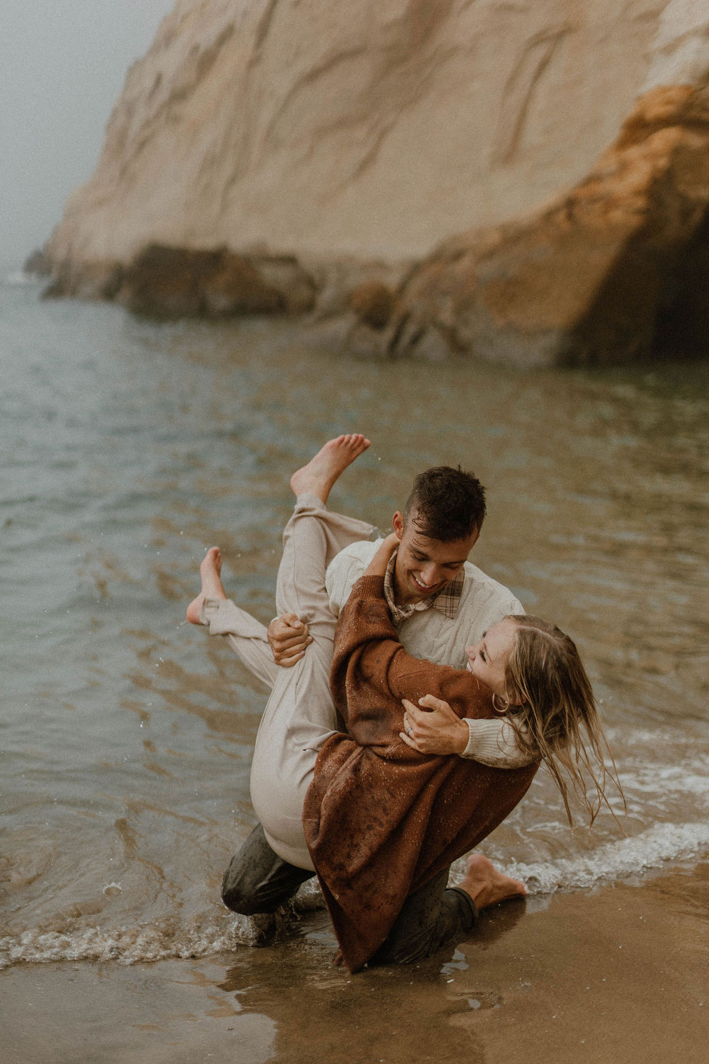 boyfriend picking up his wife in the water in their clothes from their Beach Oregon Photoshoot