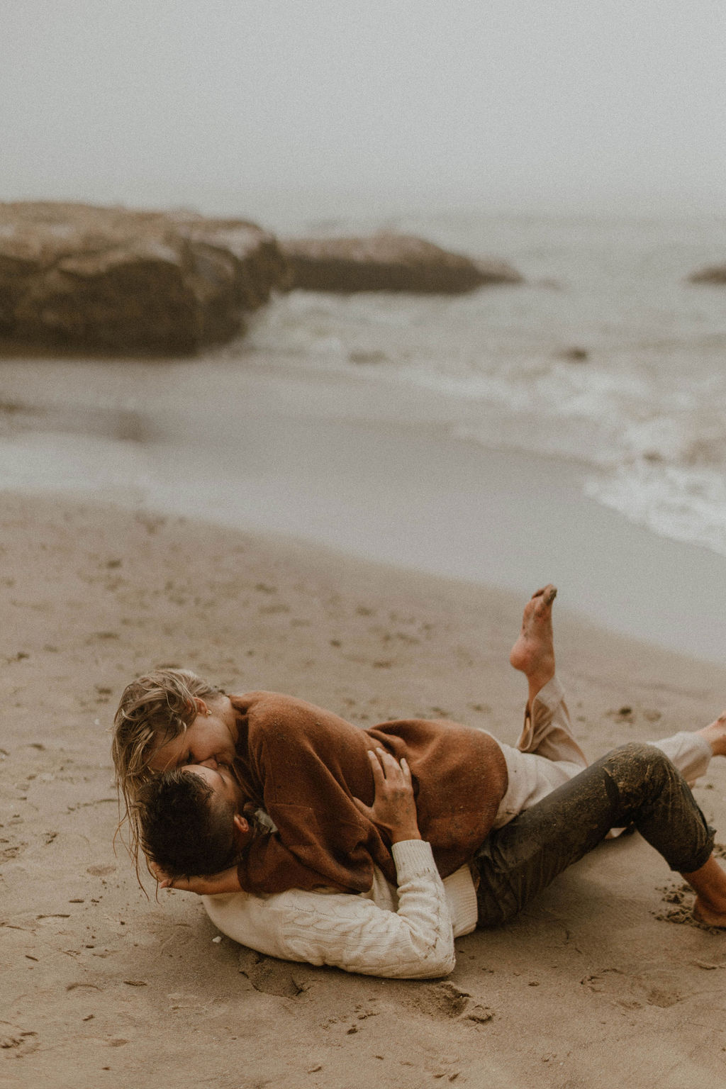 couple rolling around in the sand at their couples photoshoot